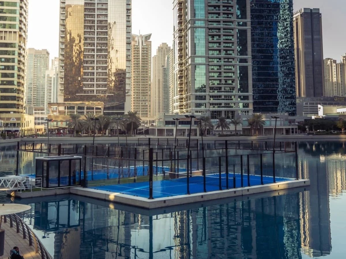 A blue padel court on the water surrounded by Dubai high-rise buildings